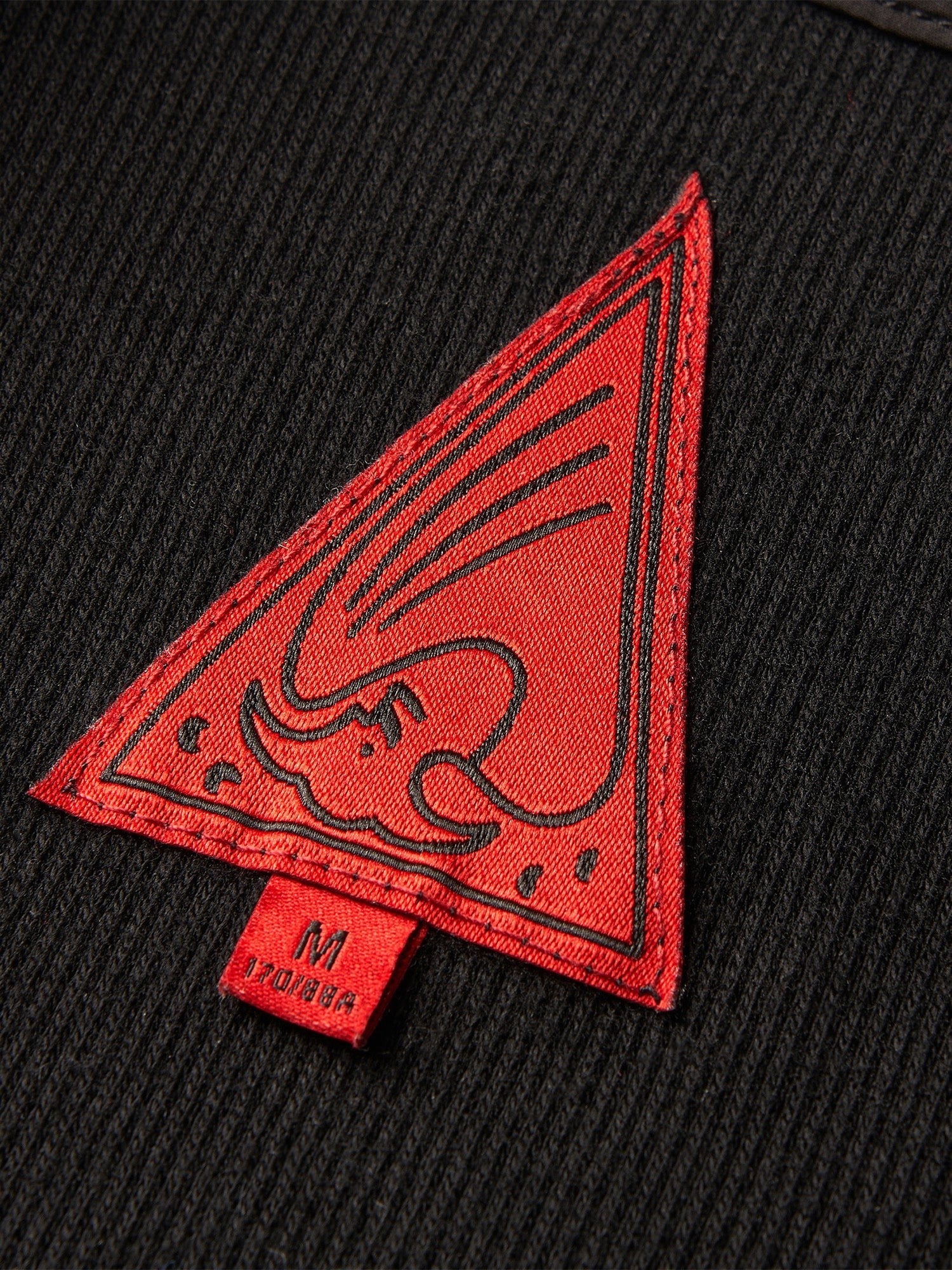 Close-up of the red triangle label on TBHNP black sword-and-bone henley tee — men's streetwear detail