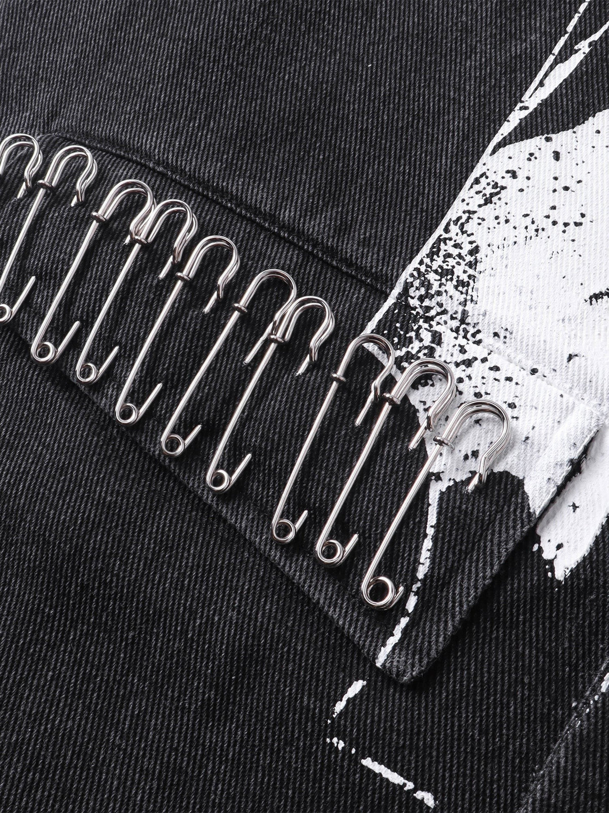 Close-up of safety pins layered over the front print on TBHNP black blazer — men's streetwear detail