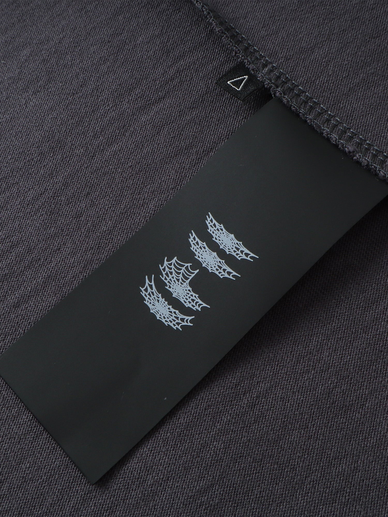 Close-up of the label on TBHNP dark grey Emblem & Shadowbat tee — men's streetwear detail