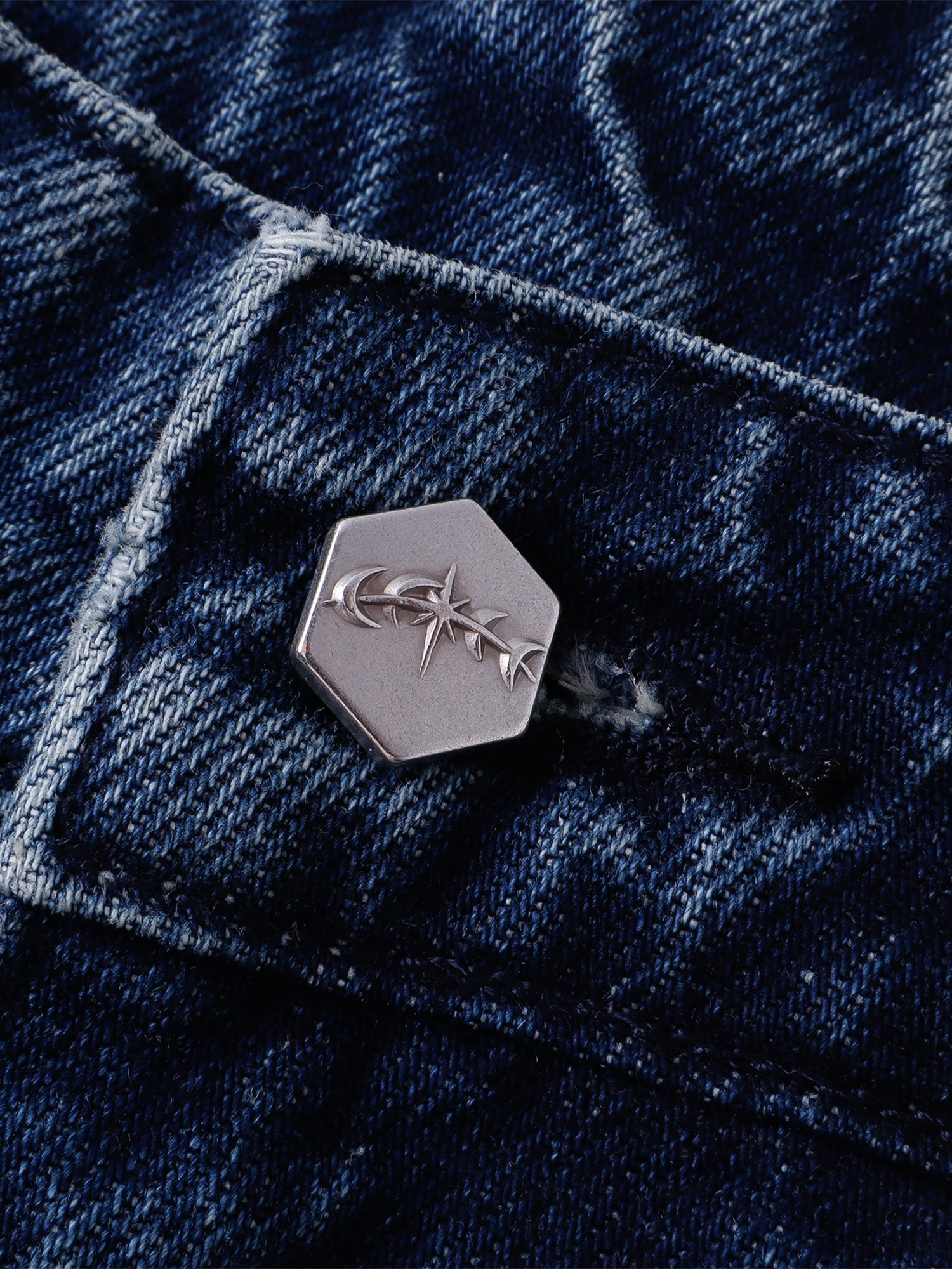 Detalle del botón hexagonal con logo astral sobre denim azul lavado