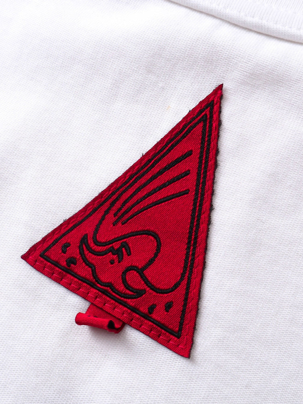 Close-up of the red triangle logo patch on TBHNP white arrival tee — men's streetwear detail