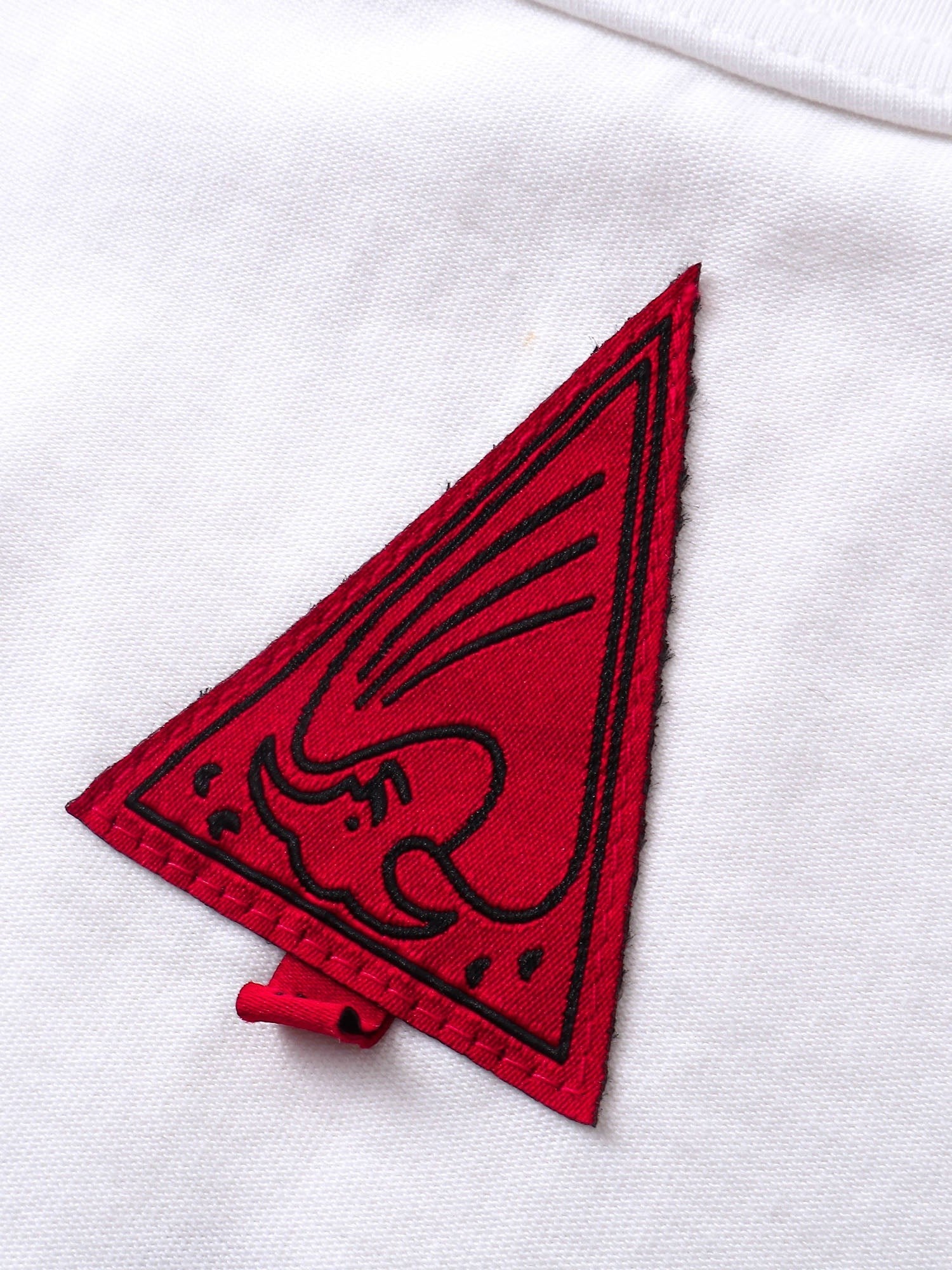 Close-up of the red triangle logo patch on TBHNP white arrival tee — men's streetwear detail