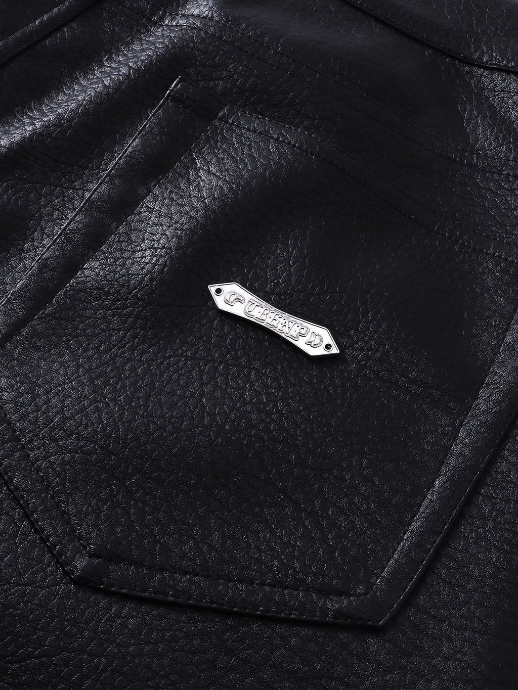 Close-up of the metal label on TBHNP black faux-leather shorts — men's streetwear detail