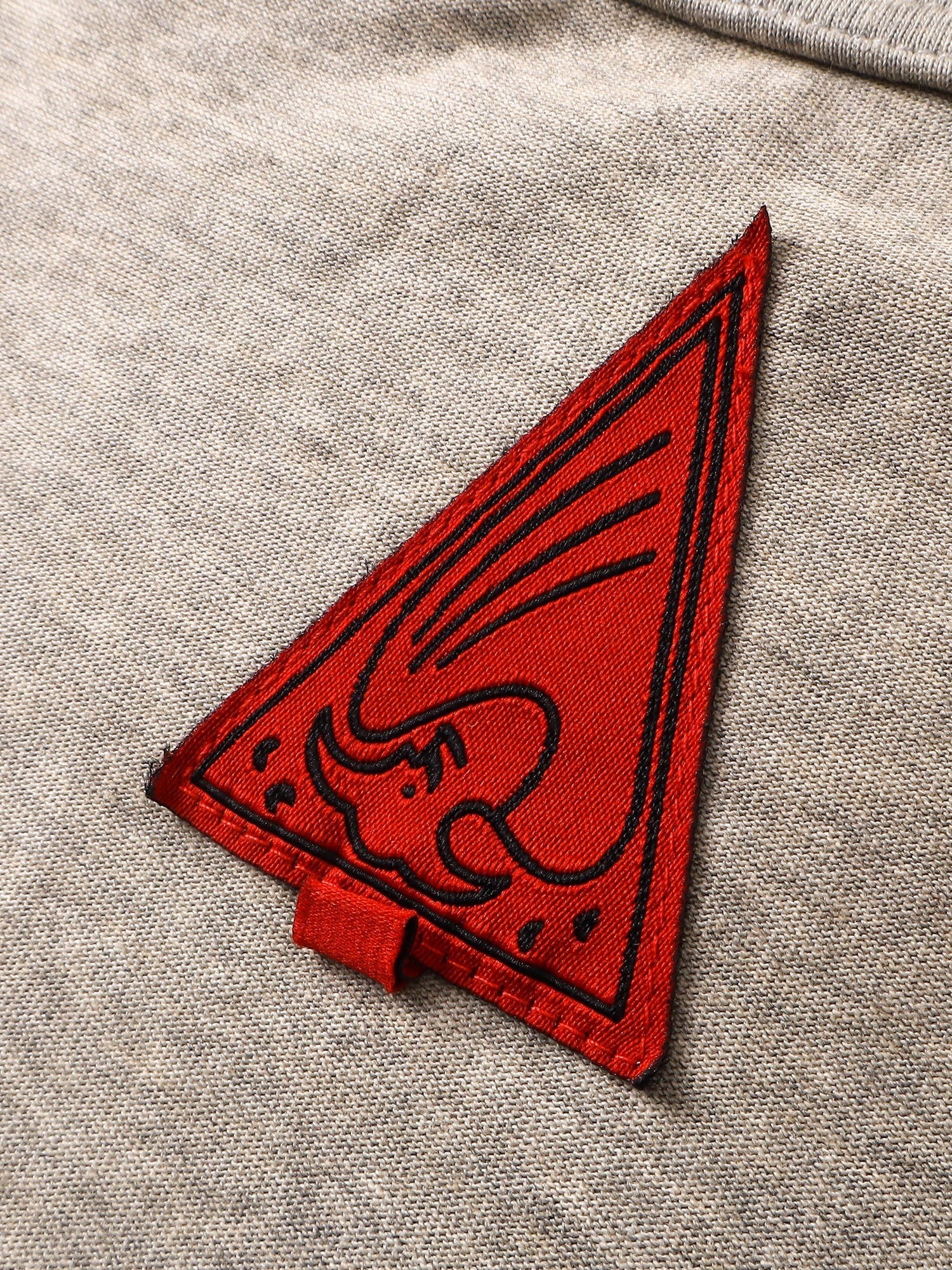 Close-up of the red triangle logo patch on TBHNP floral-grey arrival tee — men's streetwear detail
