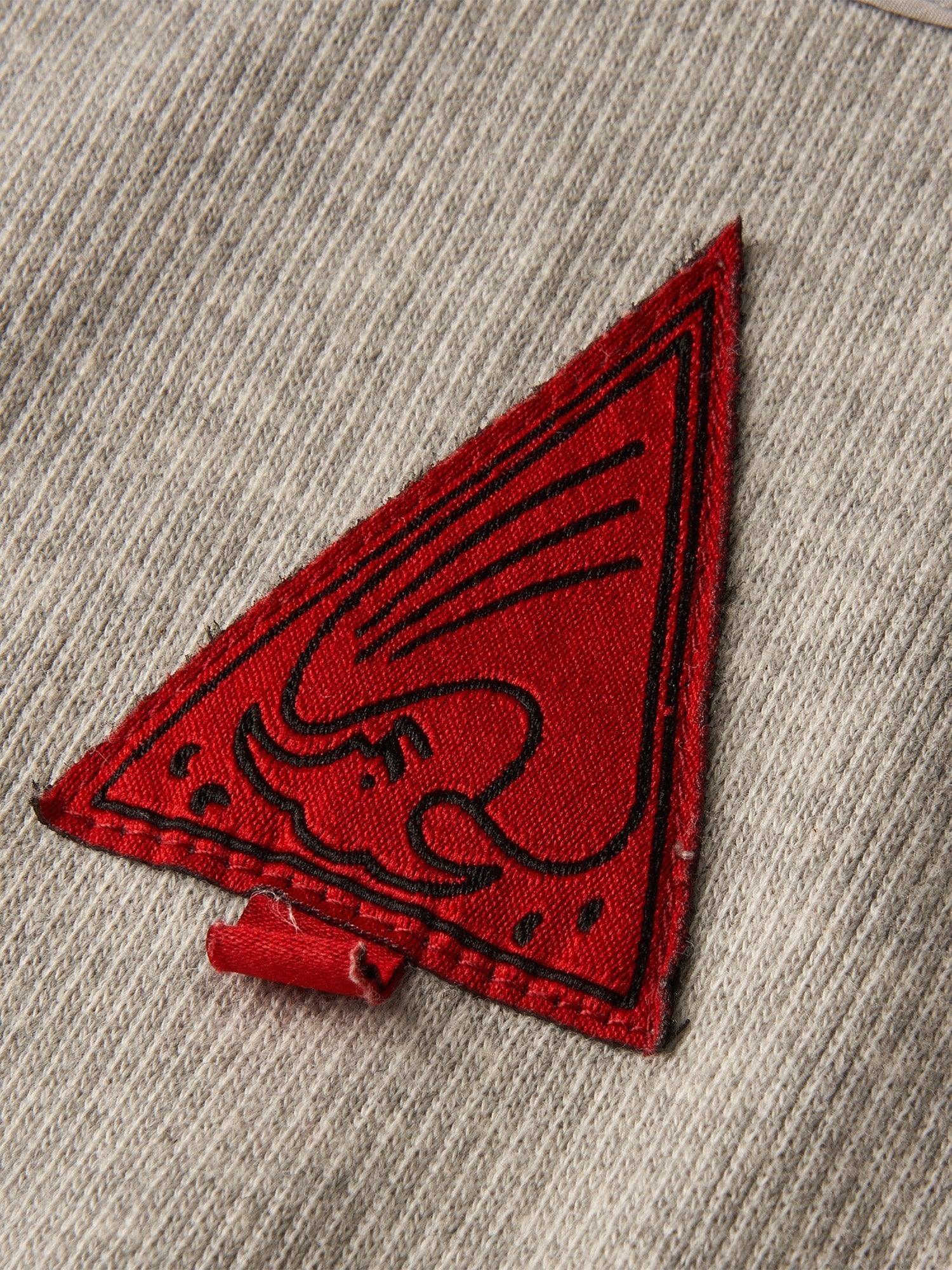 Close-up of the red triangle woven label on TBHNP sword-and-bone henley tee — men's streetwear detail
