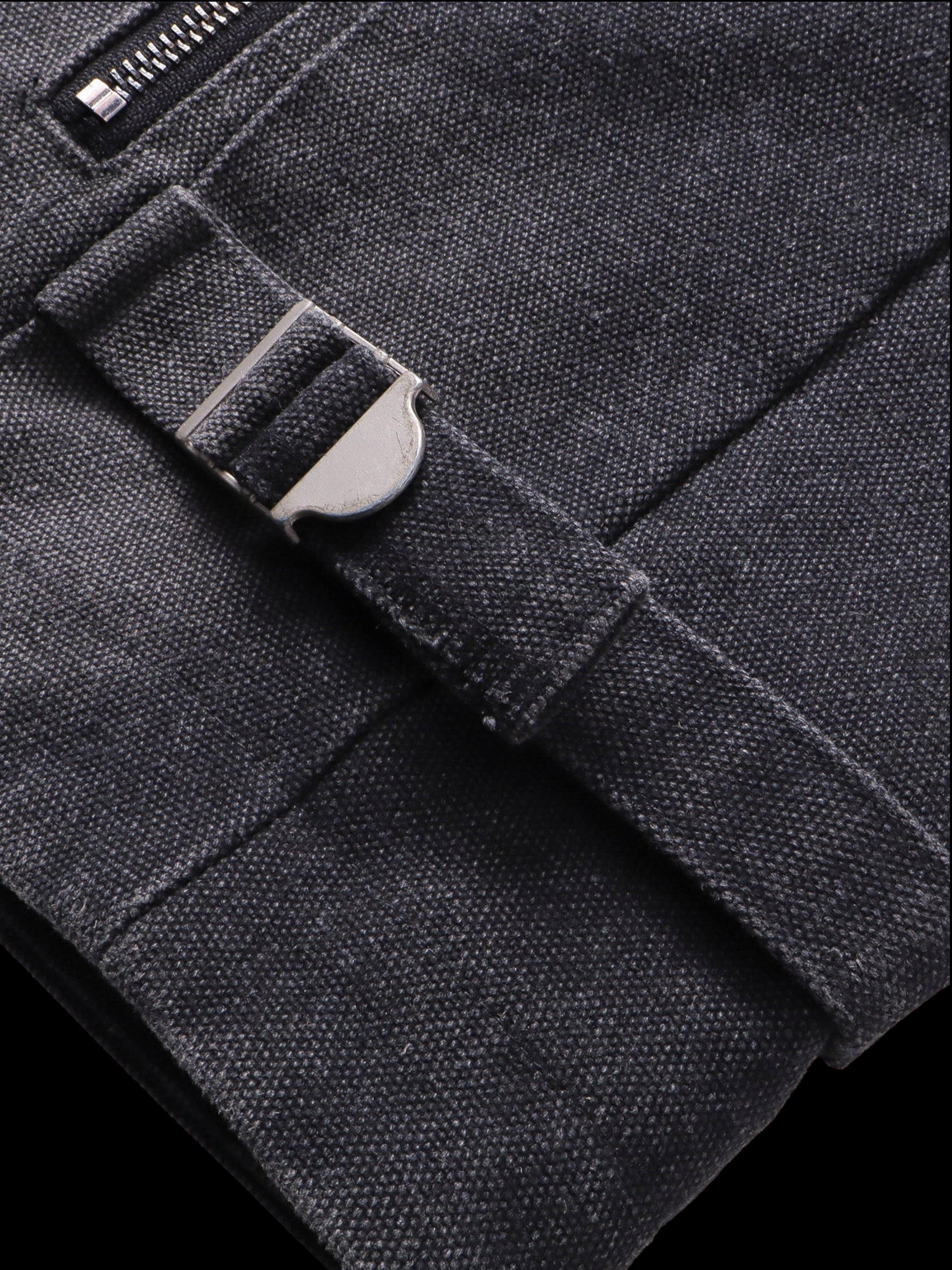 Close-up of the buckle hem adjuster tab on TBHNP black canvas moto jacket — men's streetwear detail