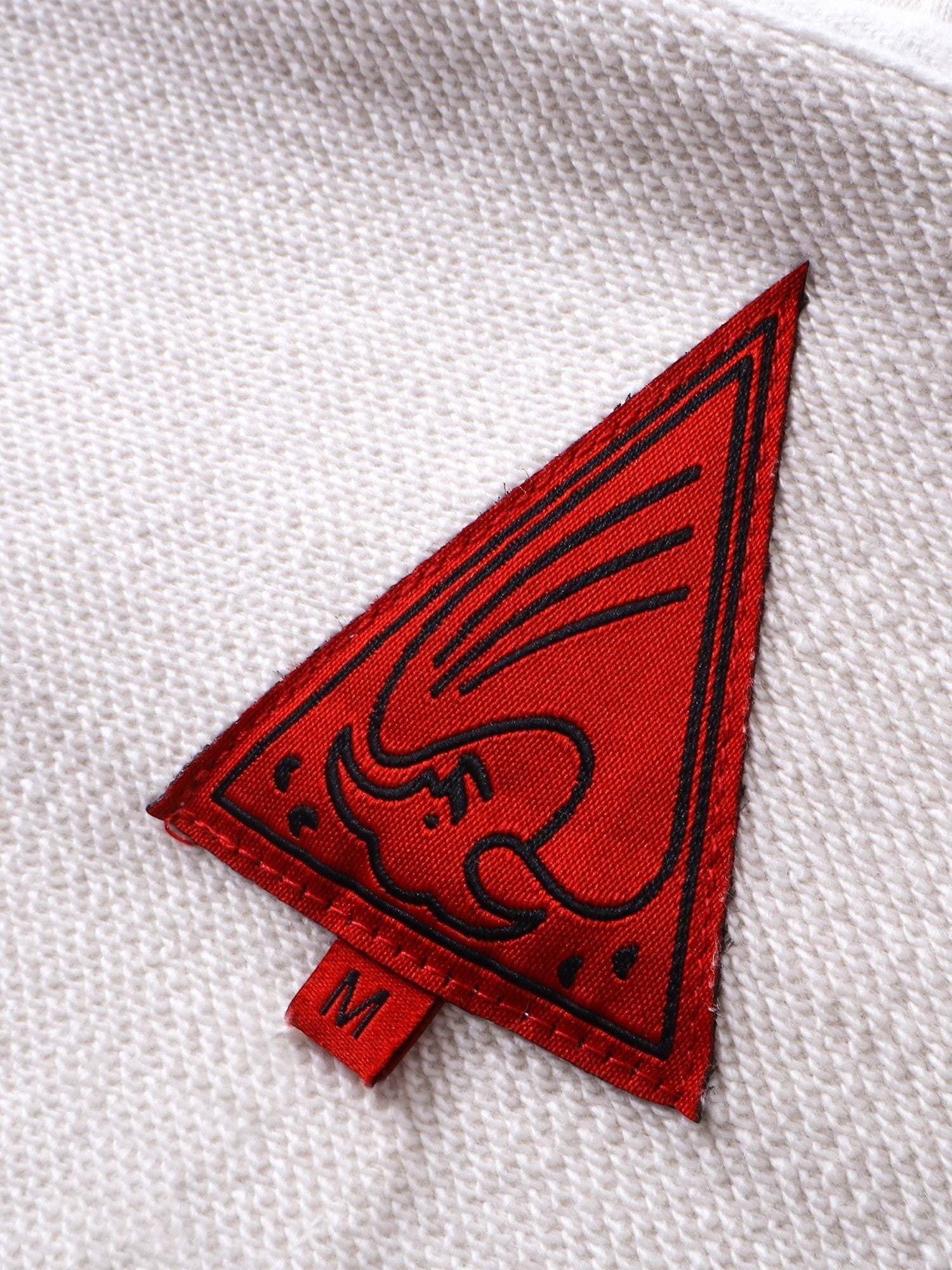 Close-up of the red triangle logo patch on TBHNP grayish-yellow hoodie — men's streetwear detail