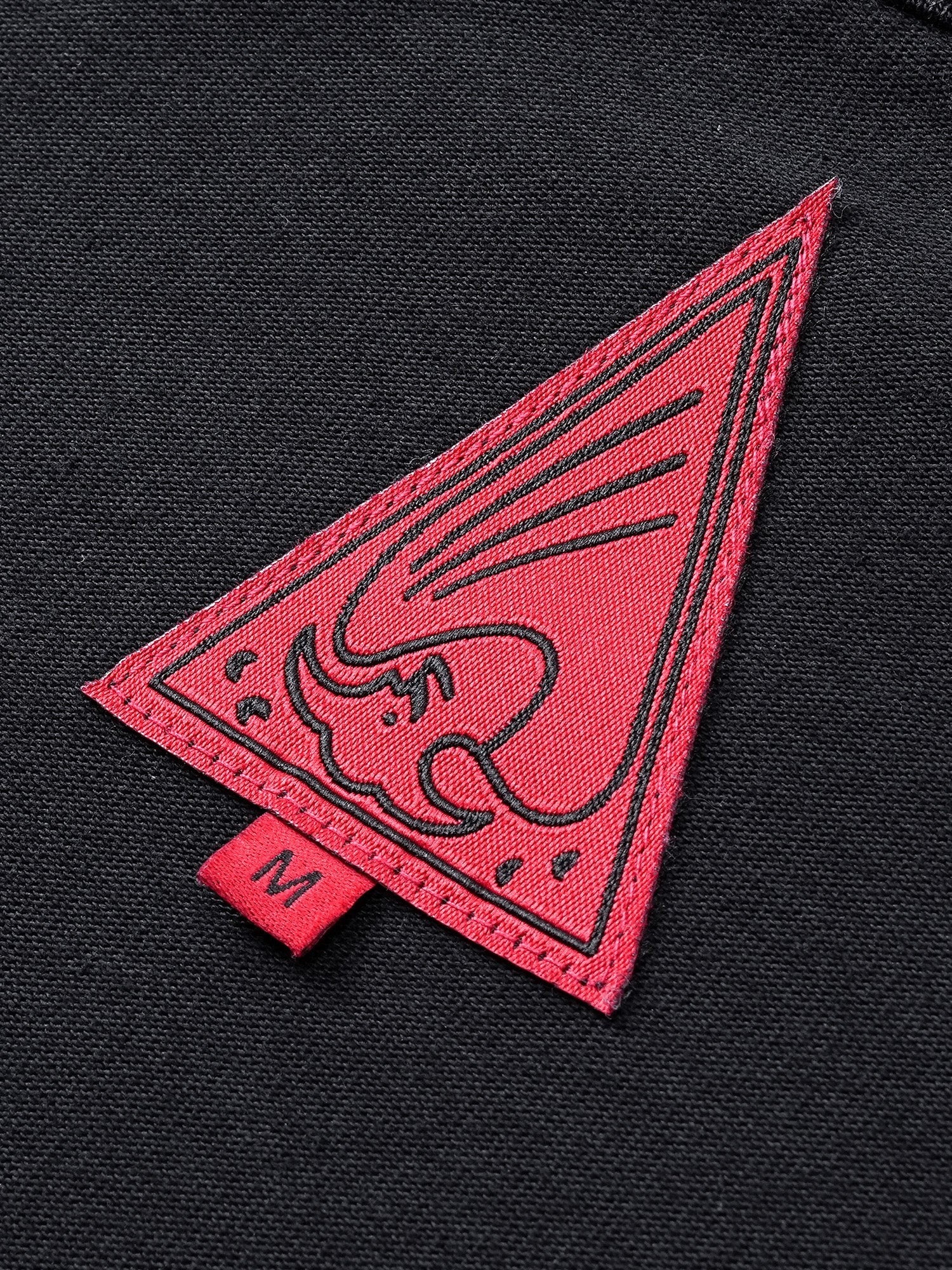 Close-up of the red triangle logo patch on TBHNP black Wraith Sorcerer tee — men's streetwear detail