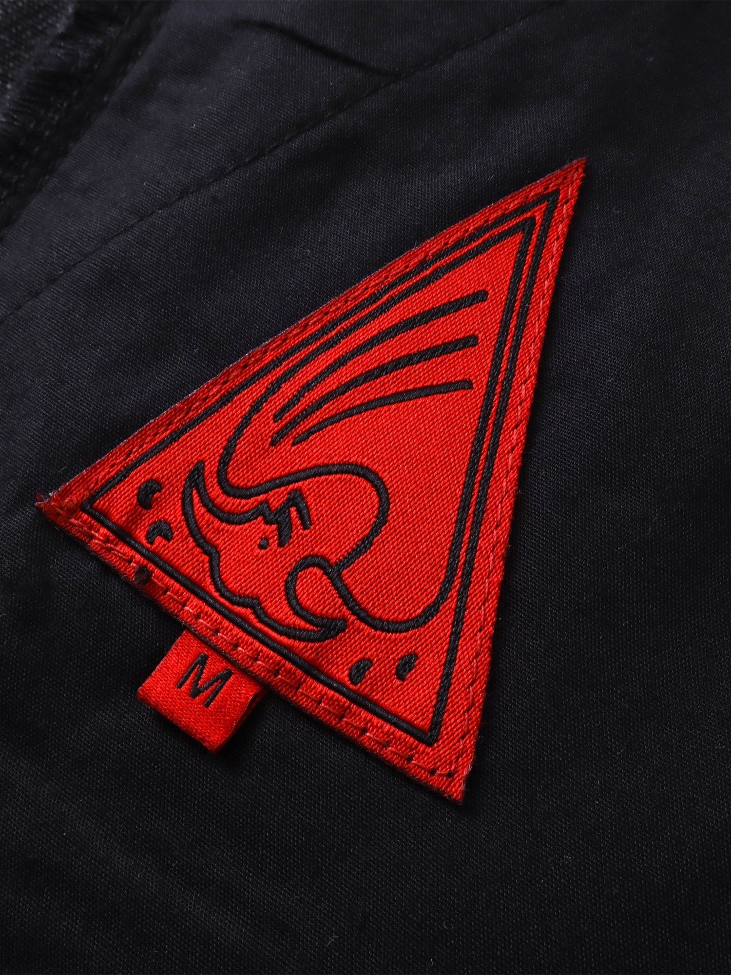 Close-up of the red triangle logo patch on TBHNP black trousers — men's streetwear detail