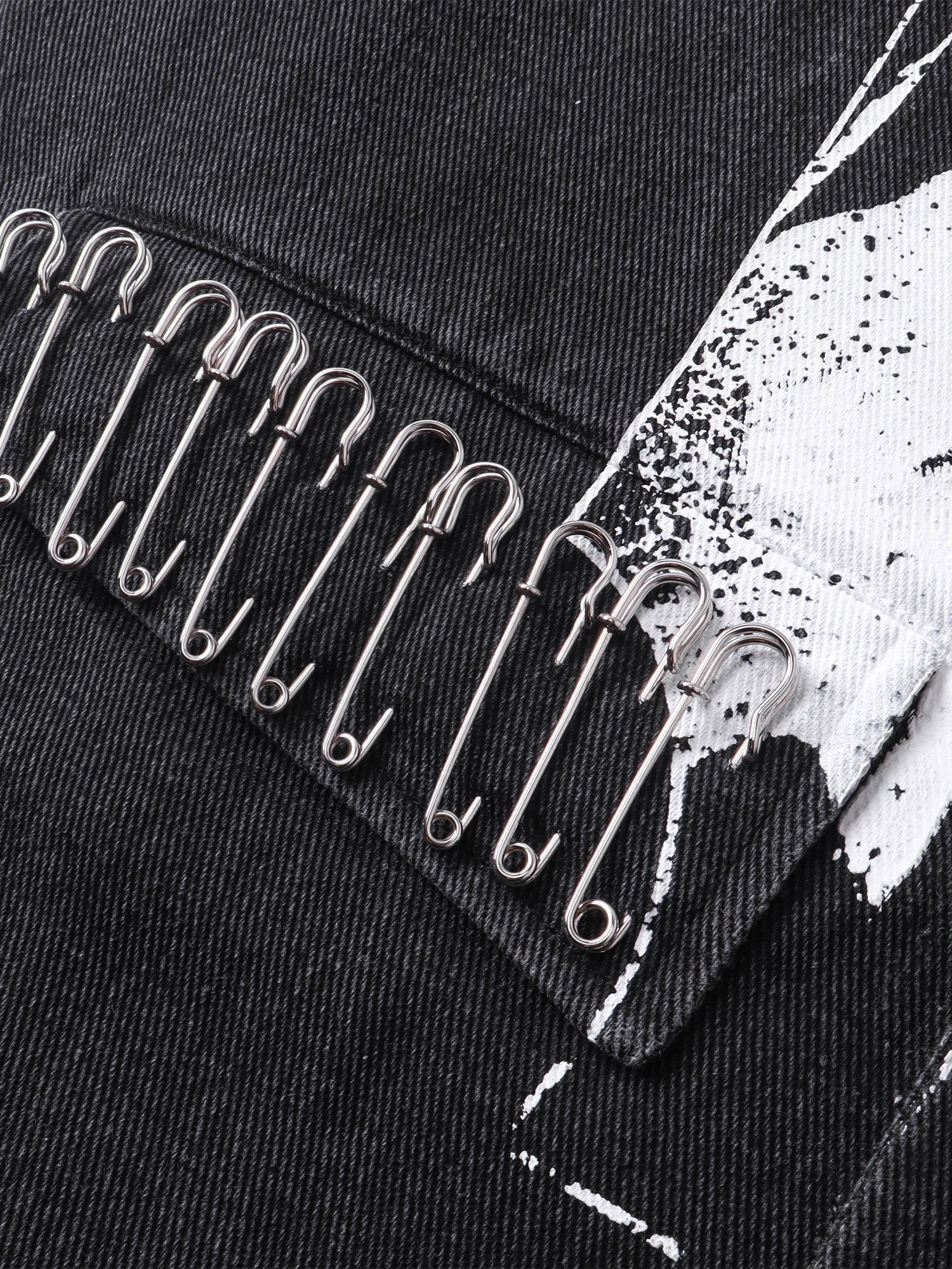 Close-up of safety pins layered over the front print on TBHNP black blazer — men's streetwear detail