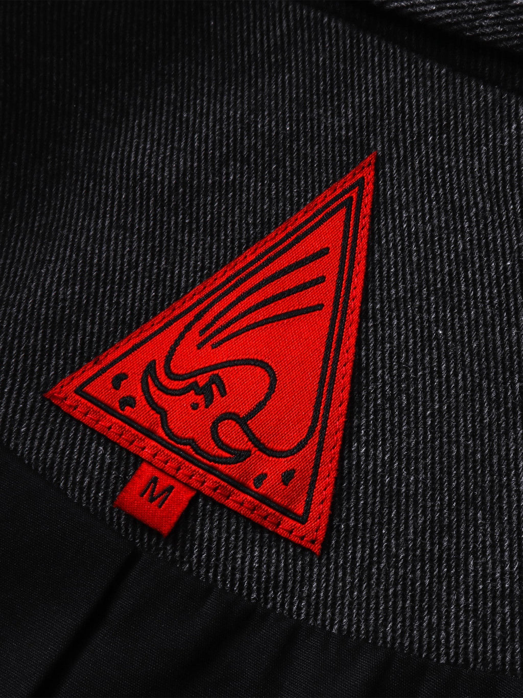 Close-up of the red triangle logo patch on TBHNP black blazer — men's streetwear detail