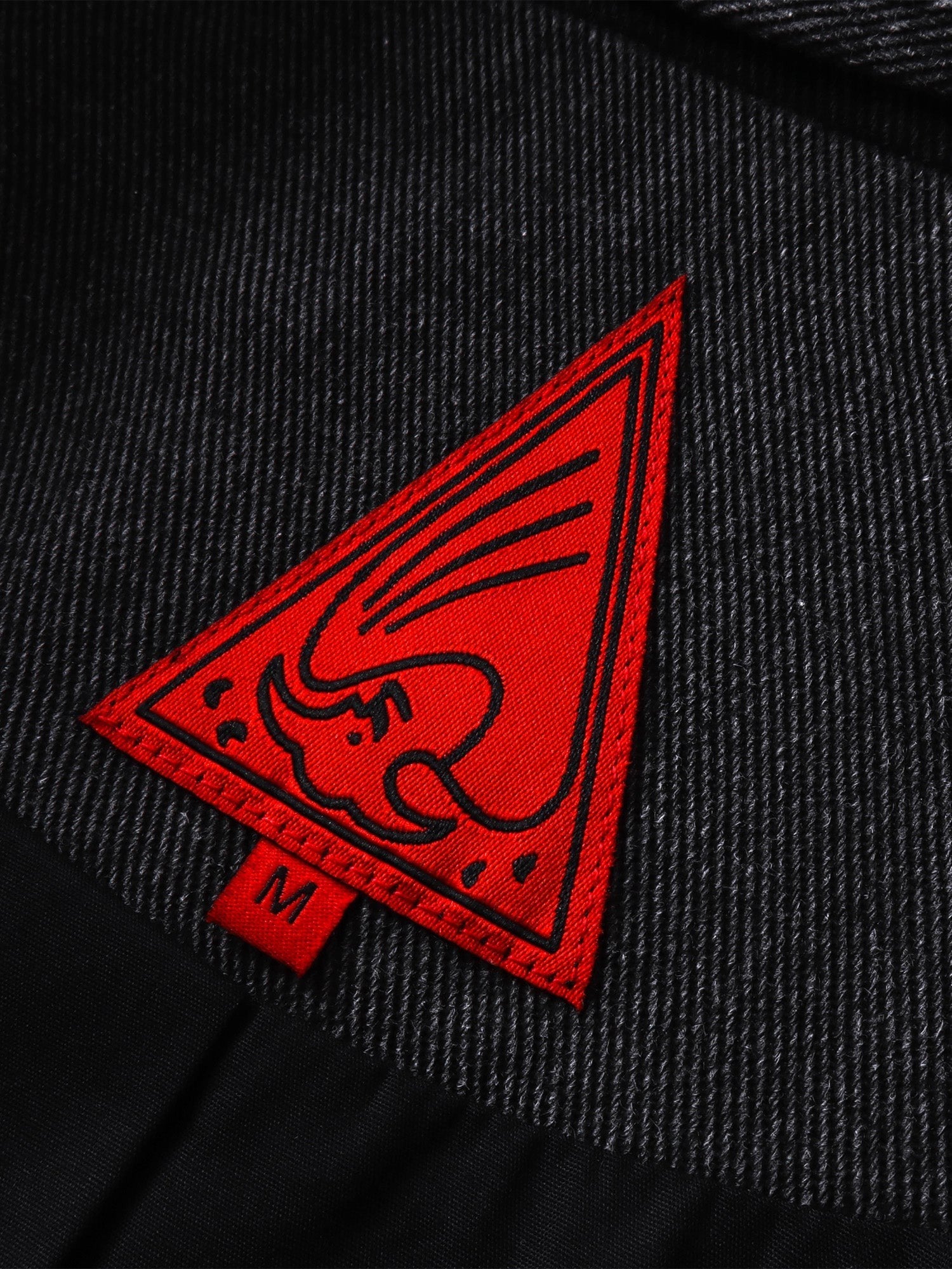 Close-up of the red triangle logo patch on TBHNP black blazer — men's streetwear detail