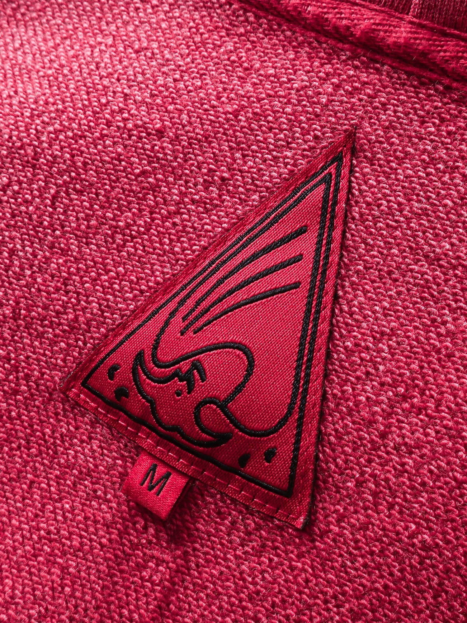 Close-up of the red triangle logo patch on TBHNP red hoodie — men's streetwear detail