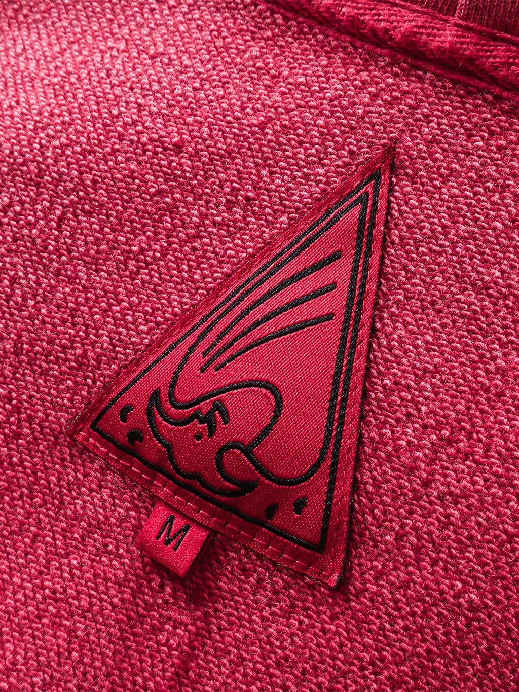 Close-up of the red triangle logo patch on TBHNP red hoodie — men's streetwear detail