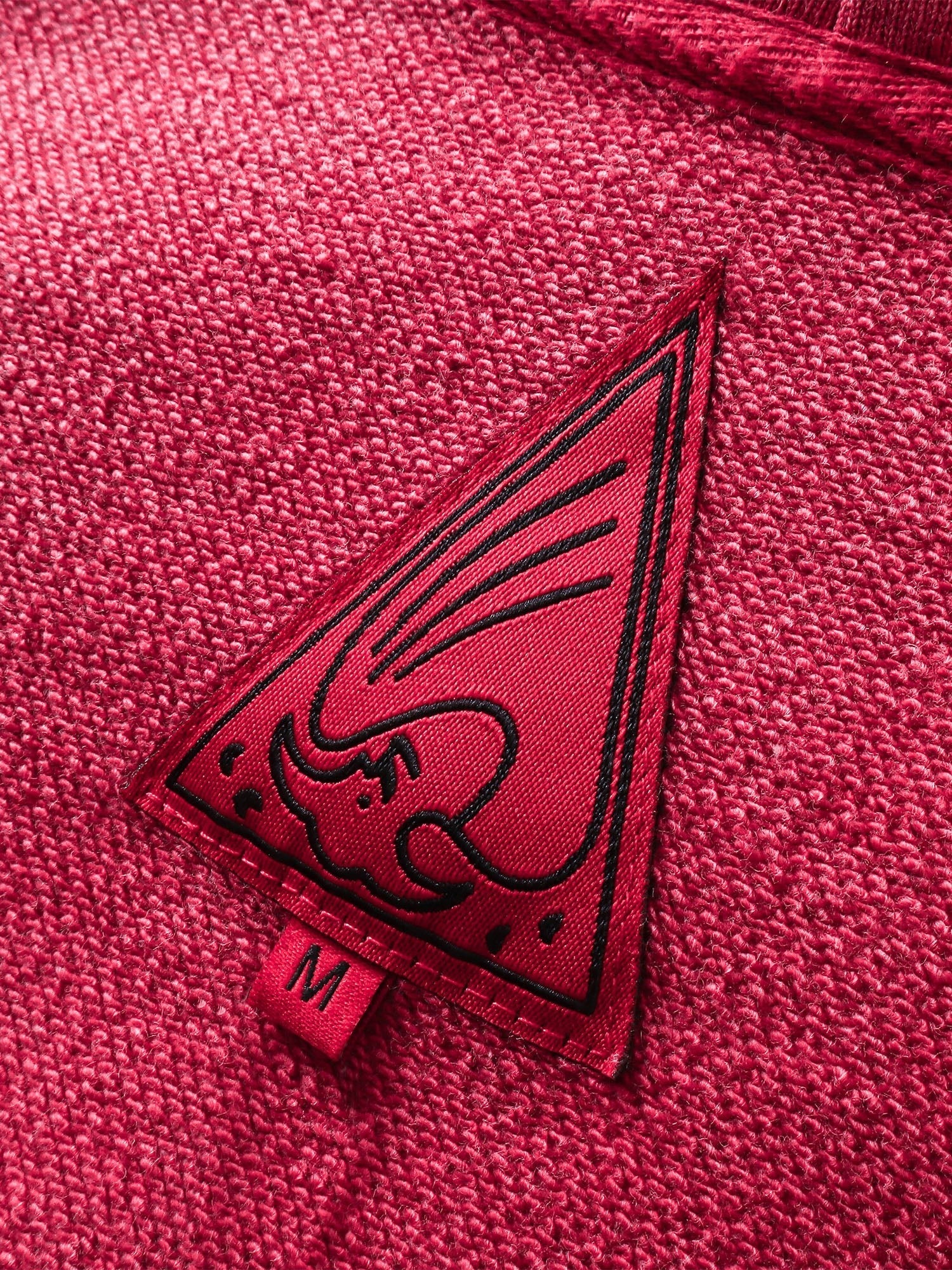 Close-up of the red triangle logo patch on TBHNP red hoodie — men's streetwear detail
