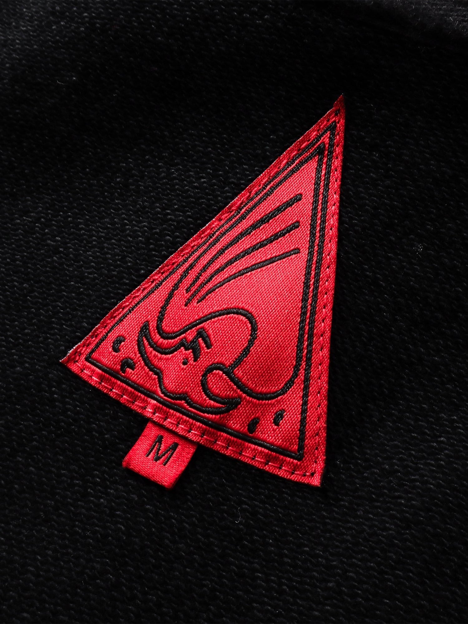 Close-up of the red triangle logo patch on TBHNP black hoodie — men's streetwear detail