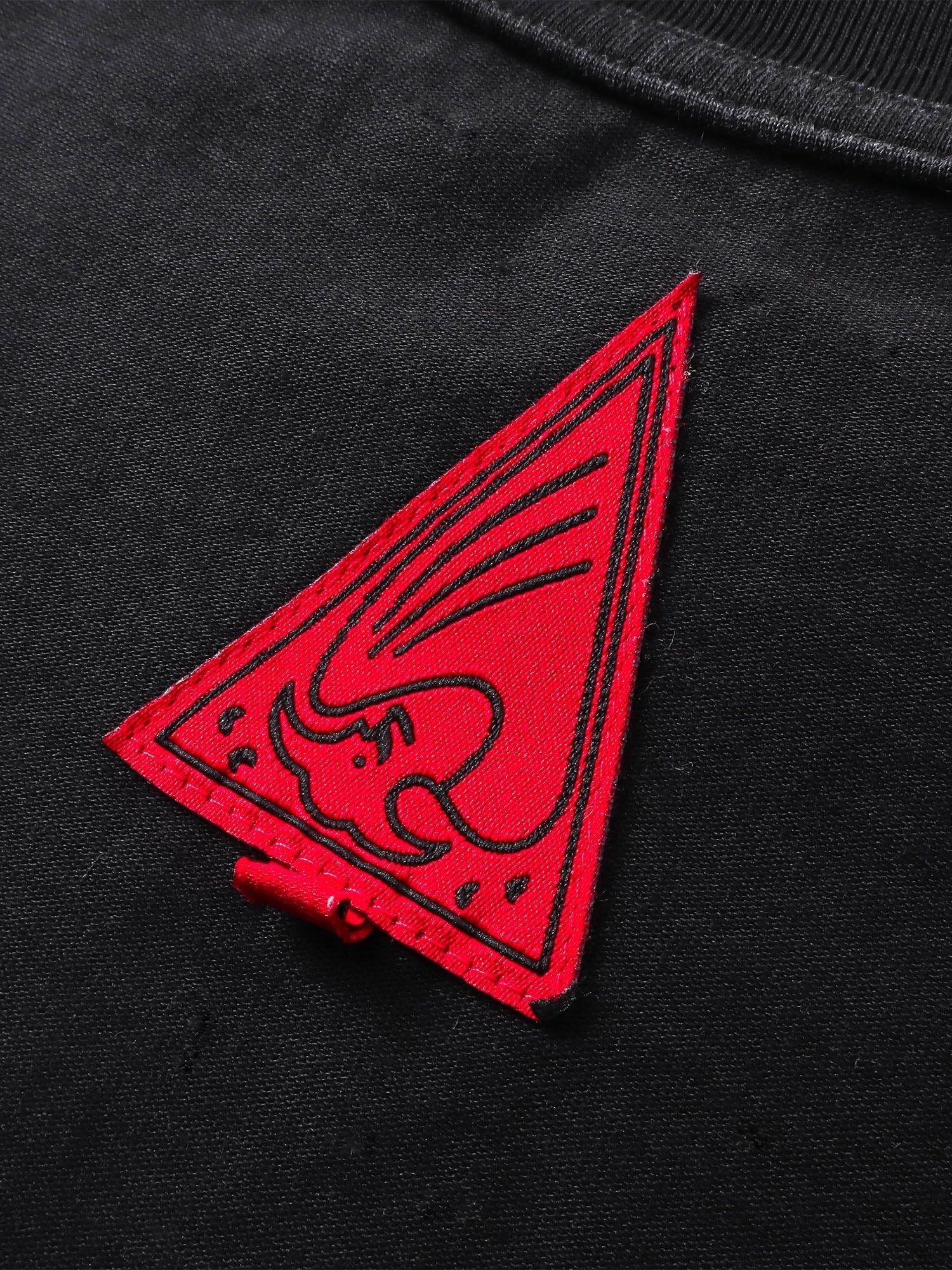 Close-up of the red triangle logo patch on TBHNP black arrival tee — men's streetwear detail