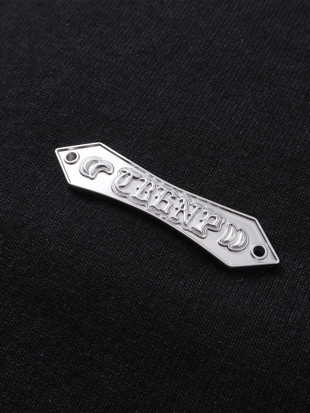 Close-up of the metal logo label on TBHNP Shadowbat vest — men's streetwear detail