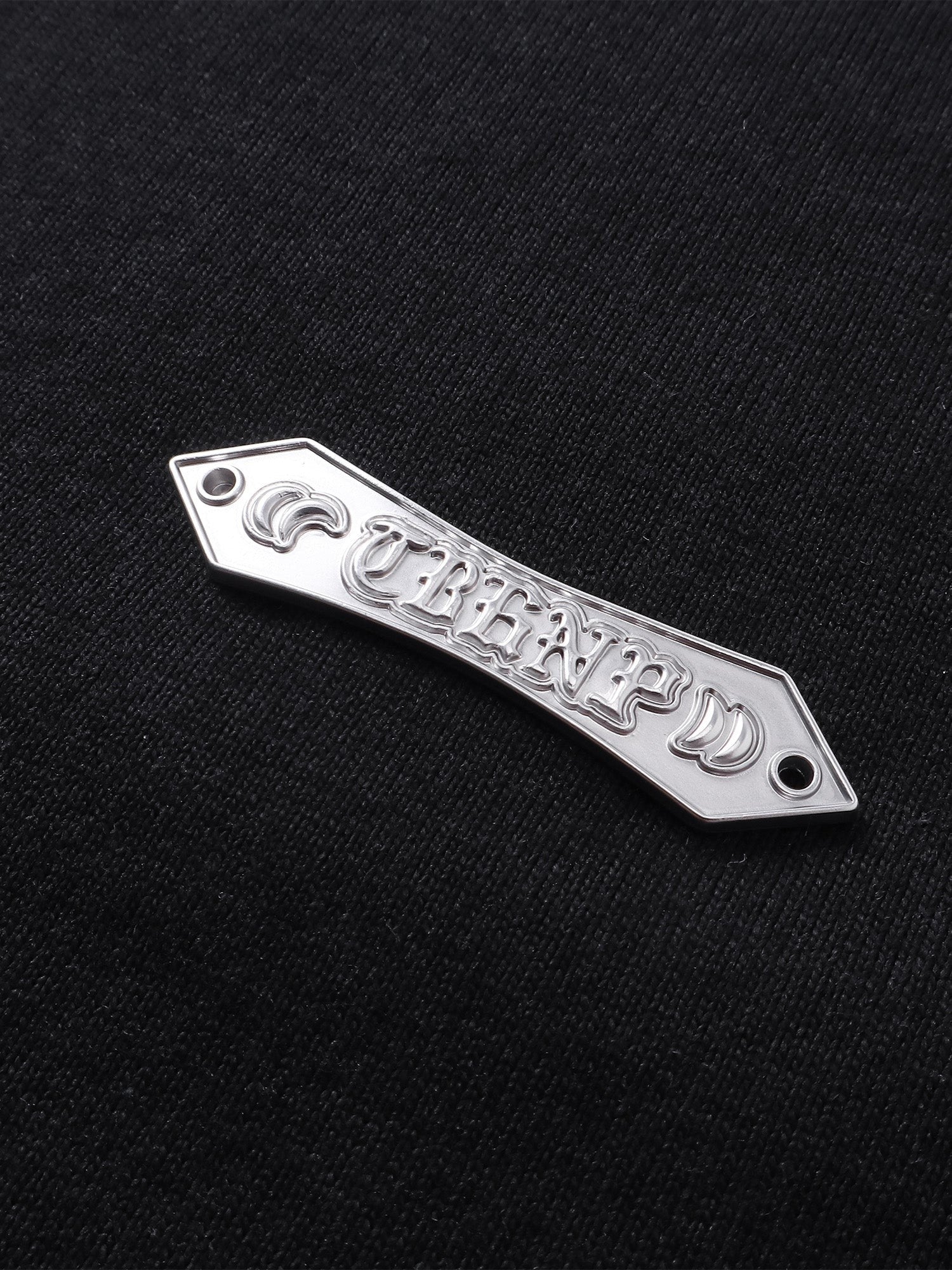 Close-up of the metal logo label on TBHNP Shadowbat vest — men's streetwear detail