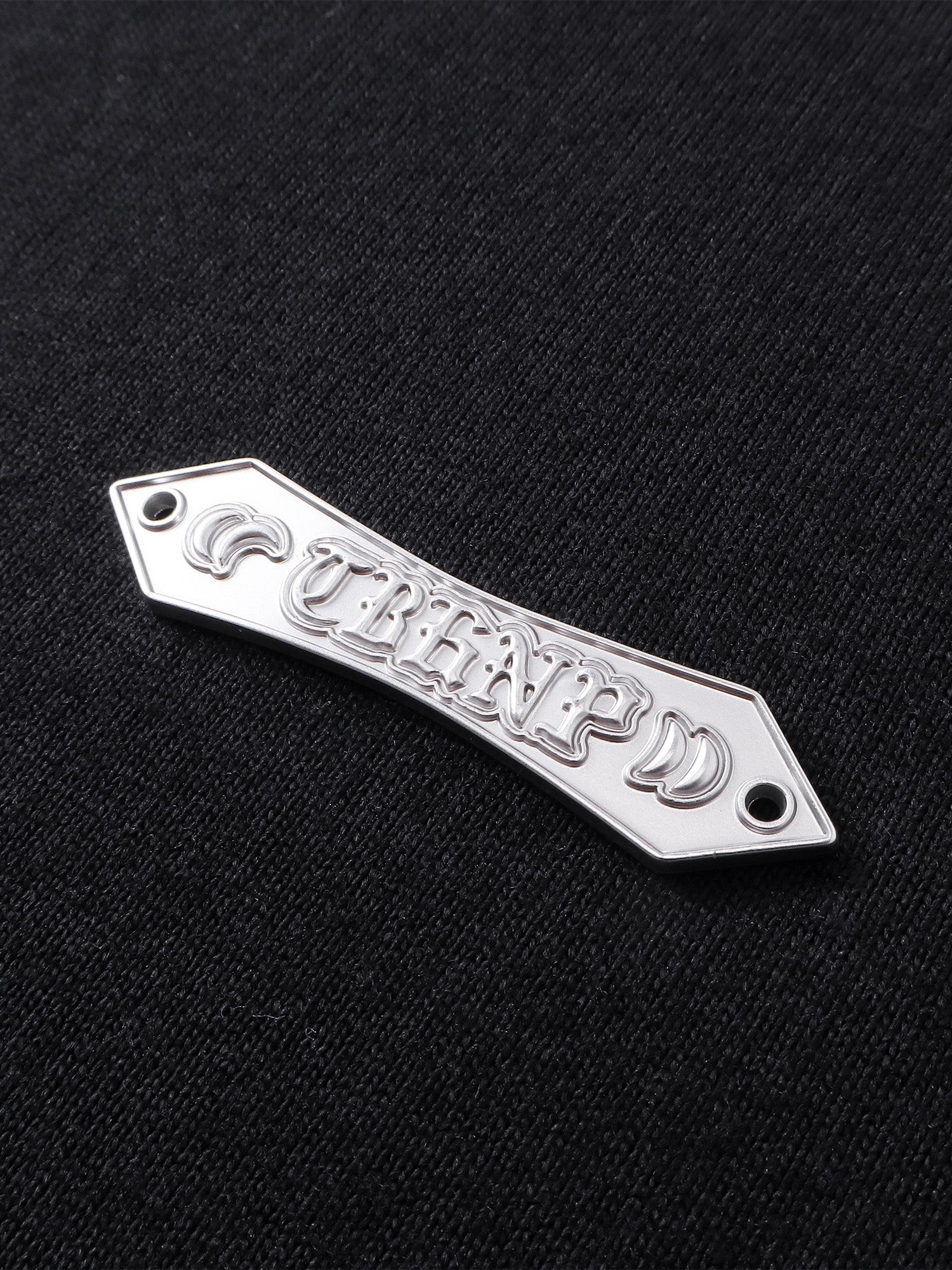 Close-up of the metal label on TBHNP black Emblem & Shadowbat tee — men's streetwear detail