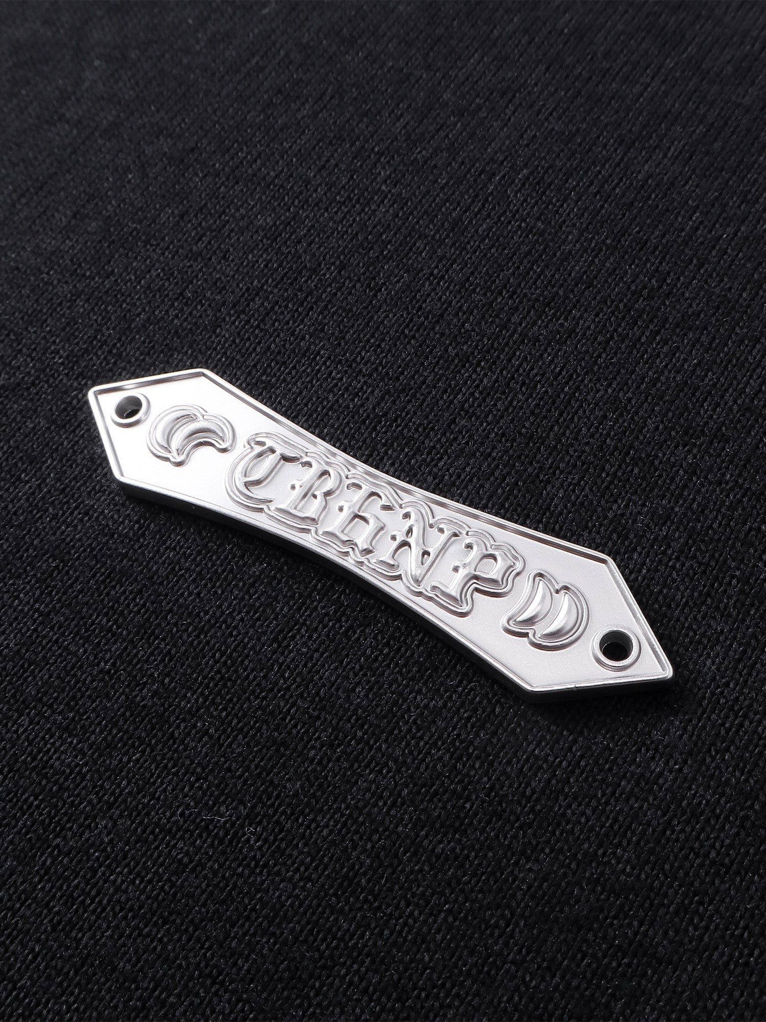 Close-up of the metal label on TBHNP black Emblem & Shadowbat tee — men's streetwear detail