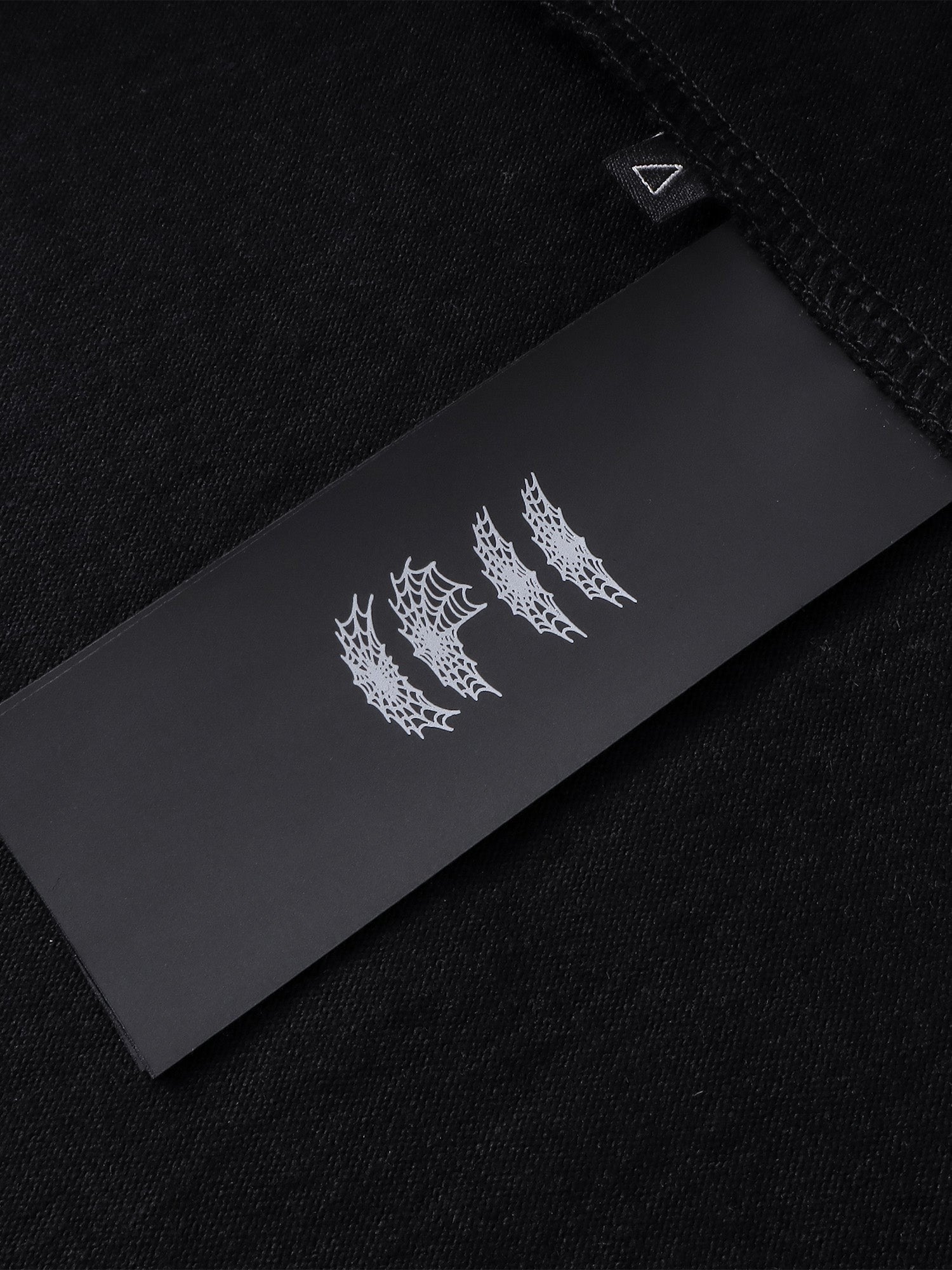Close-up of the woven label on TBHNP black Emblem & Shadowbat tee — men's streetwear detail