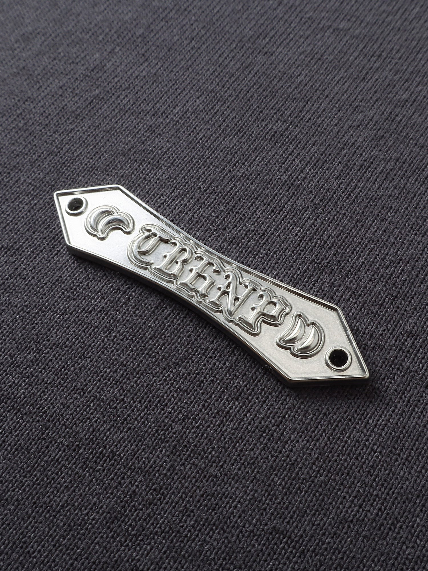 Close-up of the metal label on TBHNP dark grey Emblem & Shadowbat tee — men's streetwear detail