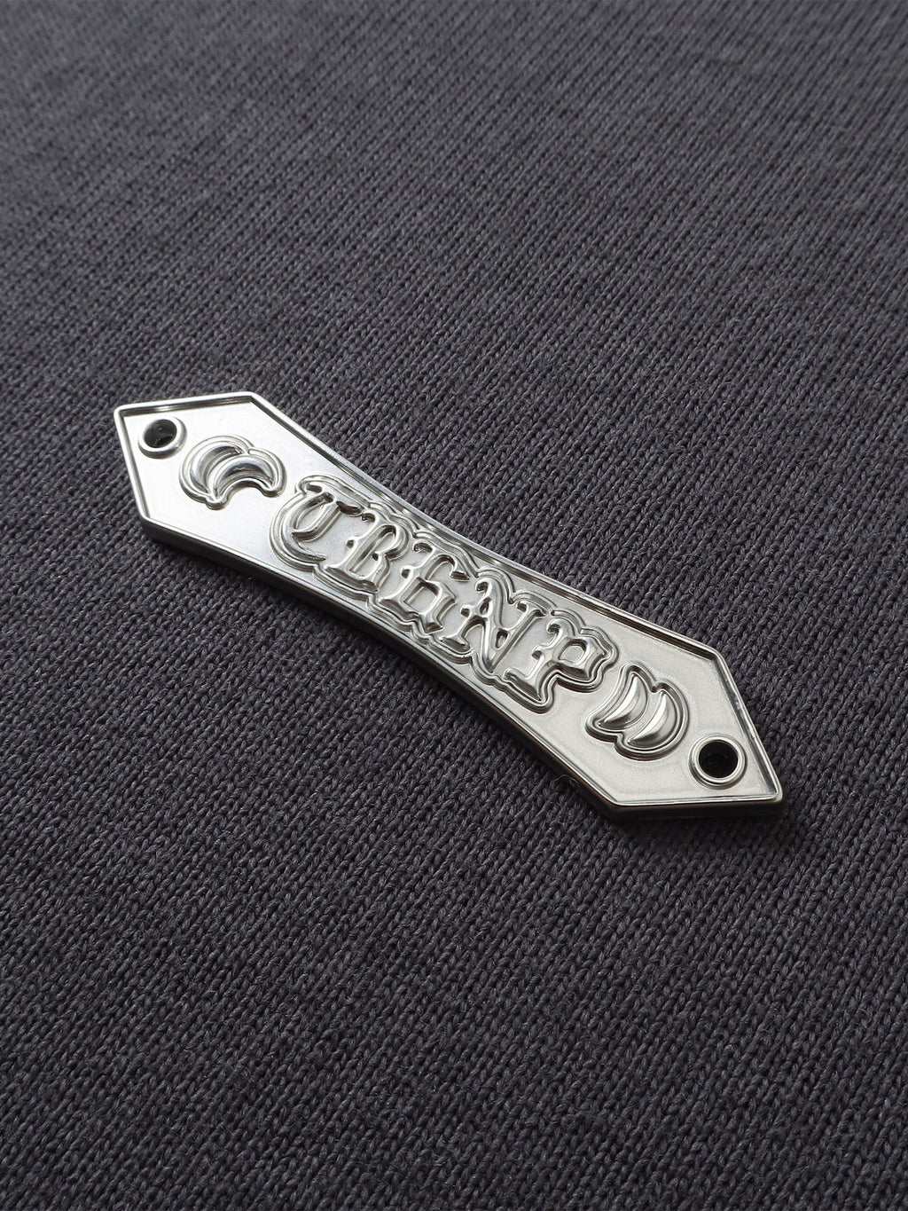 Close-up of the metal label on TBHNP dark grey Emblem & Shadowbat tee — men's streetwear detail