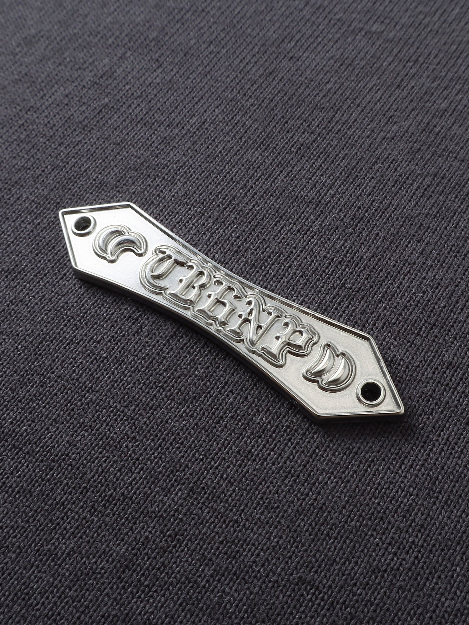 Close-up of the metal label on TBHNP dark grey Emblem & Shadowbat tee — men's streetwear detail