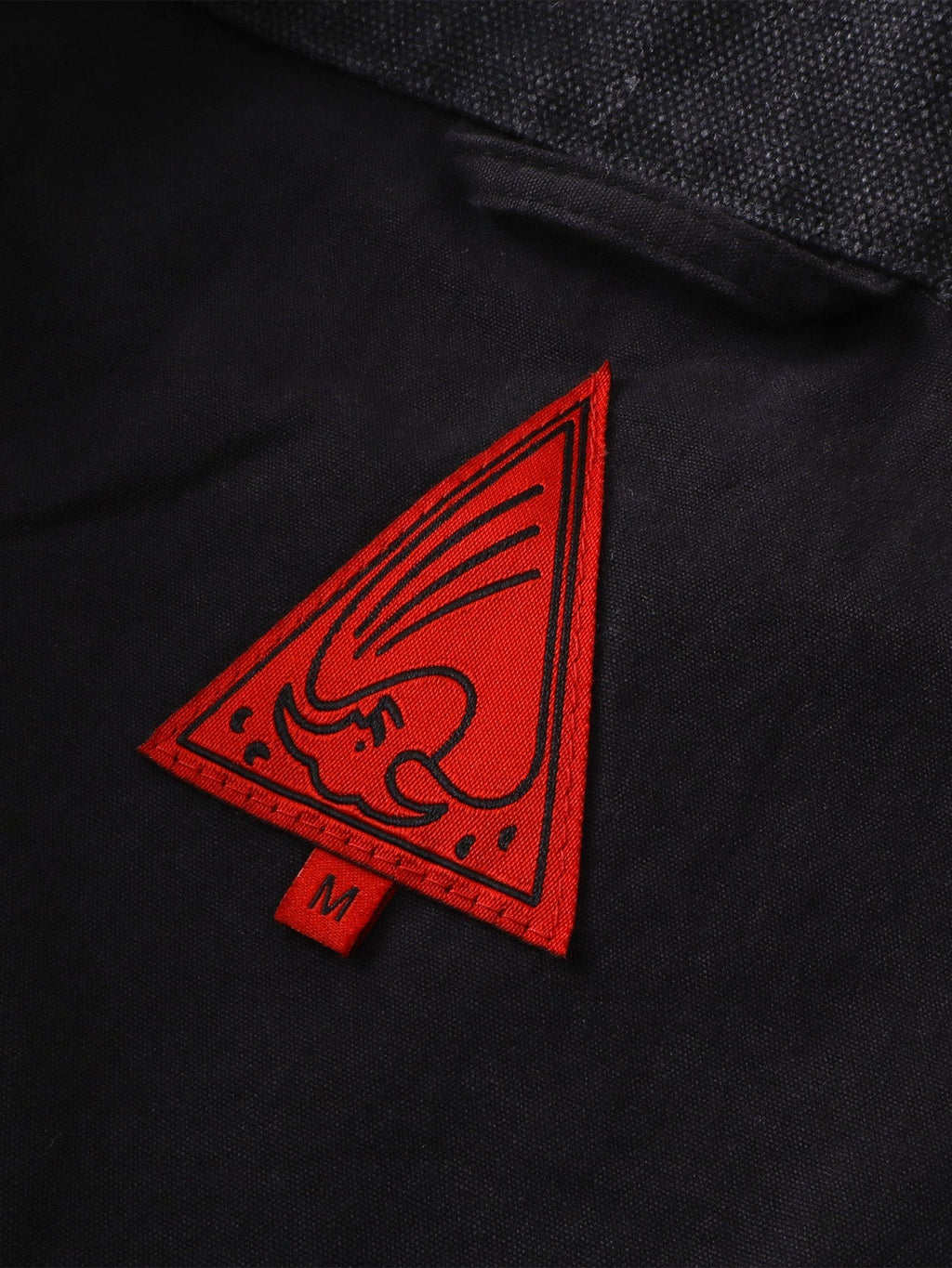 Close-up of the red triangle logo patch on TBHNP canvas moto jacket — men's streetwear detail