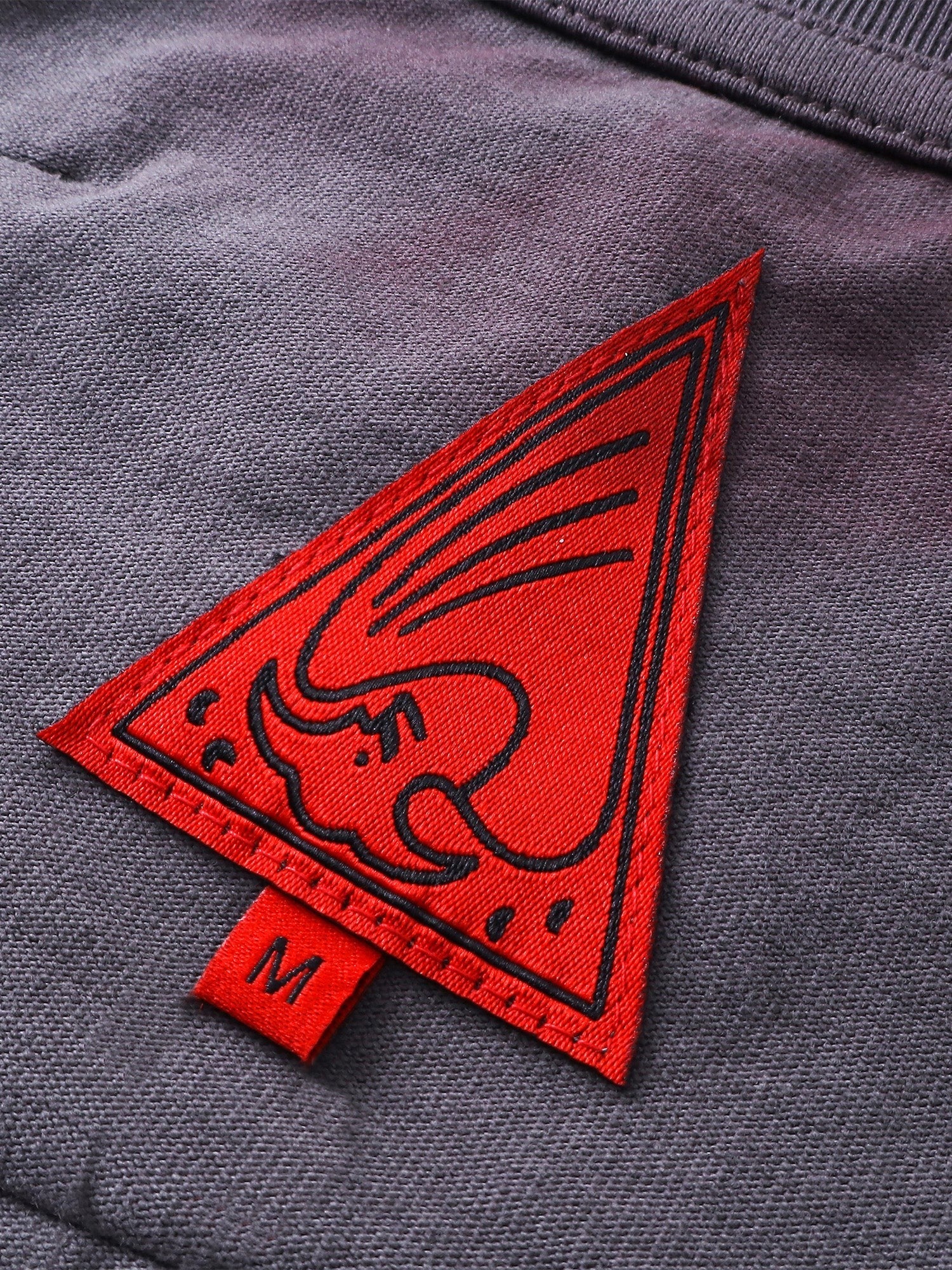 Close-up of the red triangle logo patch on TBHNP sword-and-bone tee — men's streetwear detail